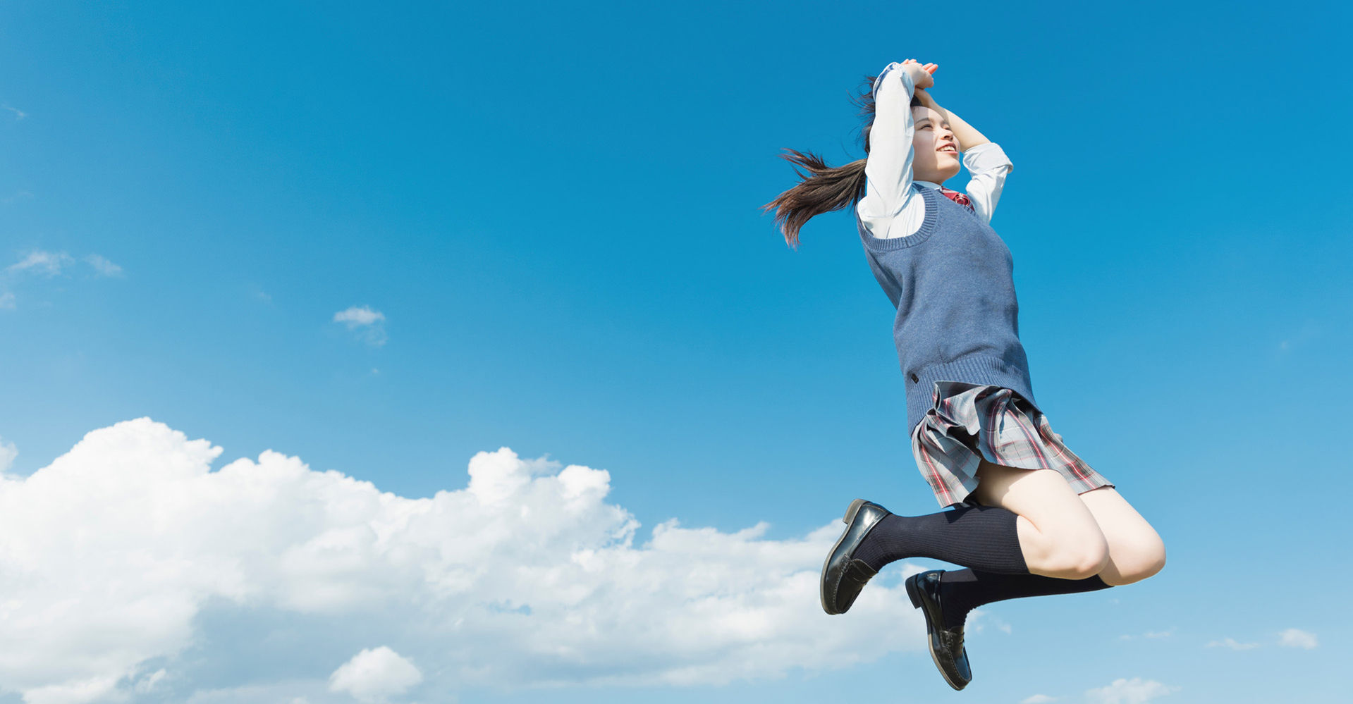 青空の下でジャンプする制服姿の生徒