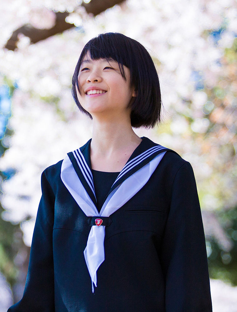桜の下で微笑むセーラー服の生徒